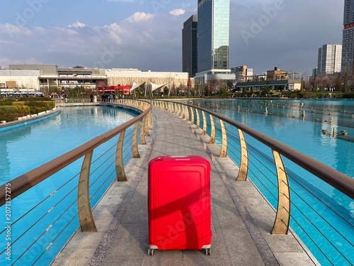 Red suitcase on modern city park bridge