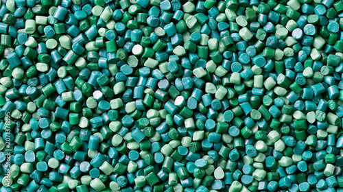 Industrial close-up of green and teal plastic pellets or granules used for recycled polymer manufacturing, injection molding, and sustainable raw material production processes.