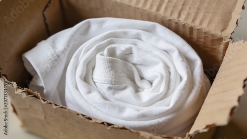 A neatly rolled white t-shirt inside a rustic cardboard shipping box, ready for delivery or unboxing.