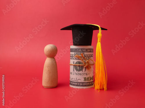A single wooden peg figure wearing a graduation cap stands next to a tied roll of dollar bills
