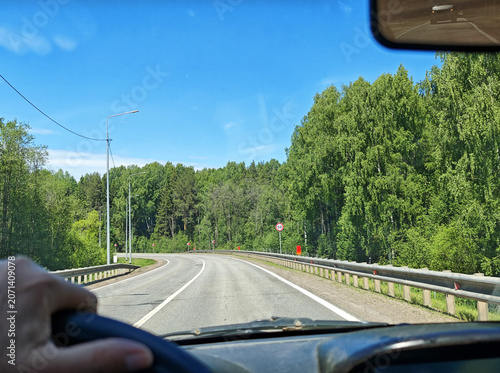 Tableau sur toile Driving on a summer road in a car with a clear view of trees and blue sky during