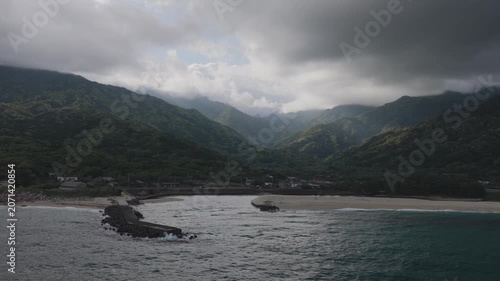 Flying over coastal river mouth with green mountains and dramatic light - Yakushima, Japan