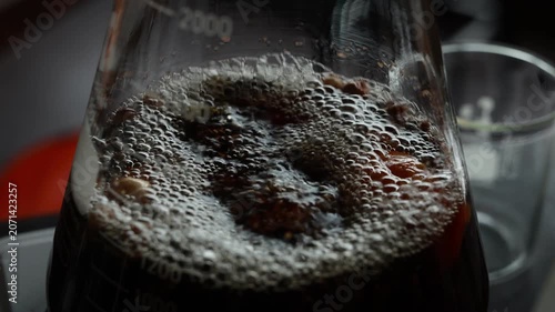 Boiling dark liquid in glass flask closeup in laboratory, bubbling surface with detailed texture, science experiment showing chemical reaction, transparent container, energetic atmosphere