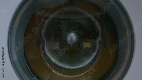 Clothing and soapy water spin around in machine. Washing machine door. Front loader