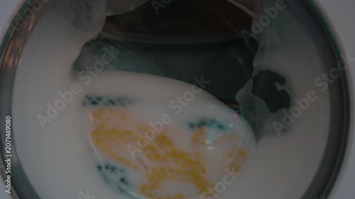 Clothing and soapy water spin around in machine. Washing machine door. Front loader