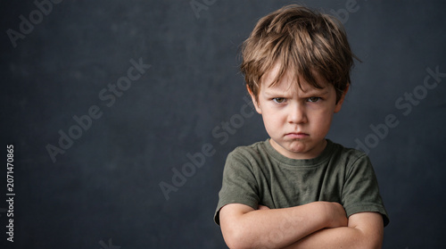 Child shows displeasure while standing with arms crossed against dark background