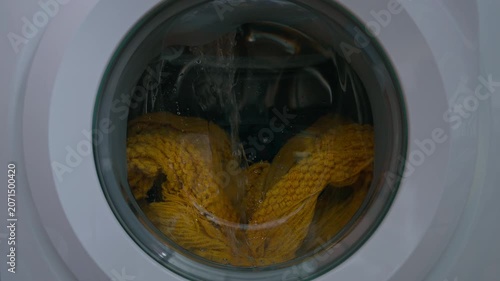 Clothing and soapy water spin around in machine. Washing machine door. Front loader