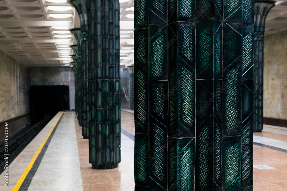 Naklejka premium Ornate green ceramic columns inside Gafur Gulom metro station in Tashkent. Empty platform with geometric tile patterns and Soviet-era architectural grandeur, ideal for travel and urban design content.
