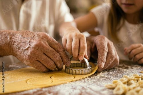 Grandfather and granddaughter hands using a round metal cutter to make pasta dough