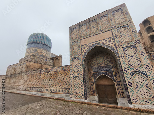 Bibi Khanum Mosque facade with turquoise dome and ornate tilework in Samarkand on an overcast day. Ideal for travel publications, heritage content, and architectural features.