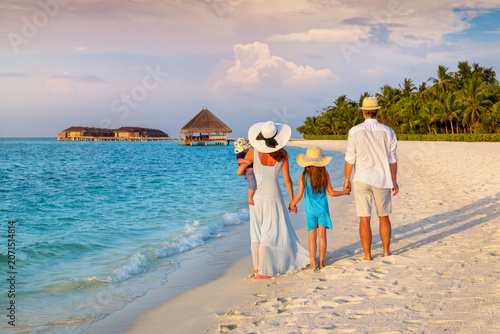 Rear view of a family on vacations looking at a tropical paradise beach in the Maldives islands during sunset time
