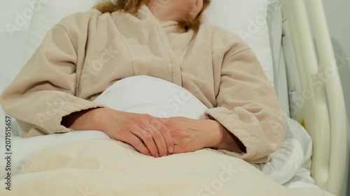 Woman patient sleeps in hospital bed with hands resting on blanket. Woman lies quietly under cover keeping fingers folded during recovery
