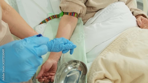 Woman doctor carefully inserts catheter into arm of patient as patient rests calmly on bed. Physician gently installs catheter. Slow motion