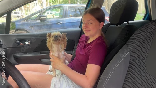 a girl with a small dog is traveling in the front seat of a car on a hot summer day, a child is sitting in a car on a hot day, traveling by car	