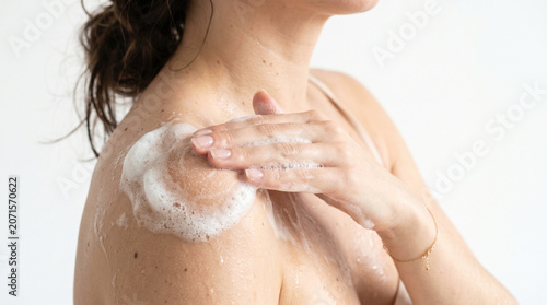 Close up of a woman washing her shoulder with thick body wash foam on white background