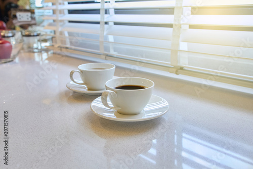 A Cup of coffee on a table next to the windows in the morning.