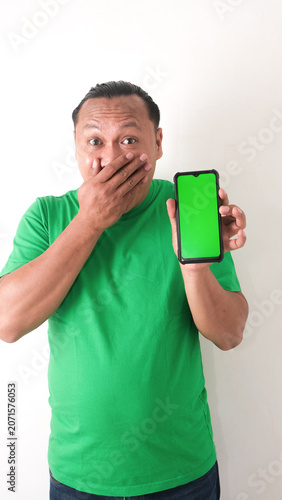 A portrait of a happy Asian man is smiling and showing copy space on his smartphone wearing green shirt isolated by a white background