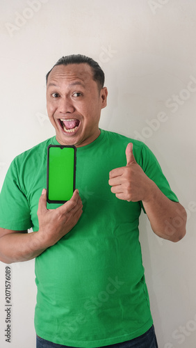 A portrait of a happy Asian man is smiling and showing copy space on his smartphone wearing green shirt isolated by a white background