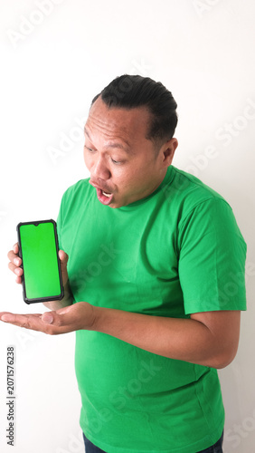 A portrait of a happy Asian man is smiling and showing copy space on his smartphone wearing green shirt isolated by a white background