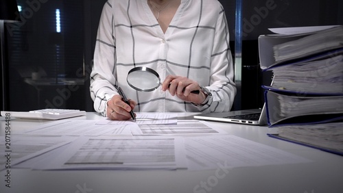 Bild auf Leinwand Professional woman uses magnifying glass and pen to scrutinize financial reports