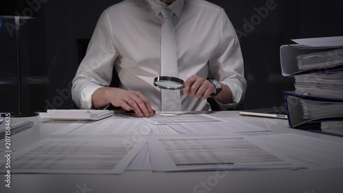 Obraz na płótnie Professional businessman using a magnifying glass discovering financial data and scrutinizing corporate tax documents