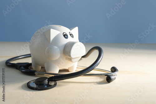Piggy bank and a medical stethoscope on light colored wood against a blue background, concept for austerity measures in the healthcare sector, copy space
