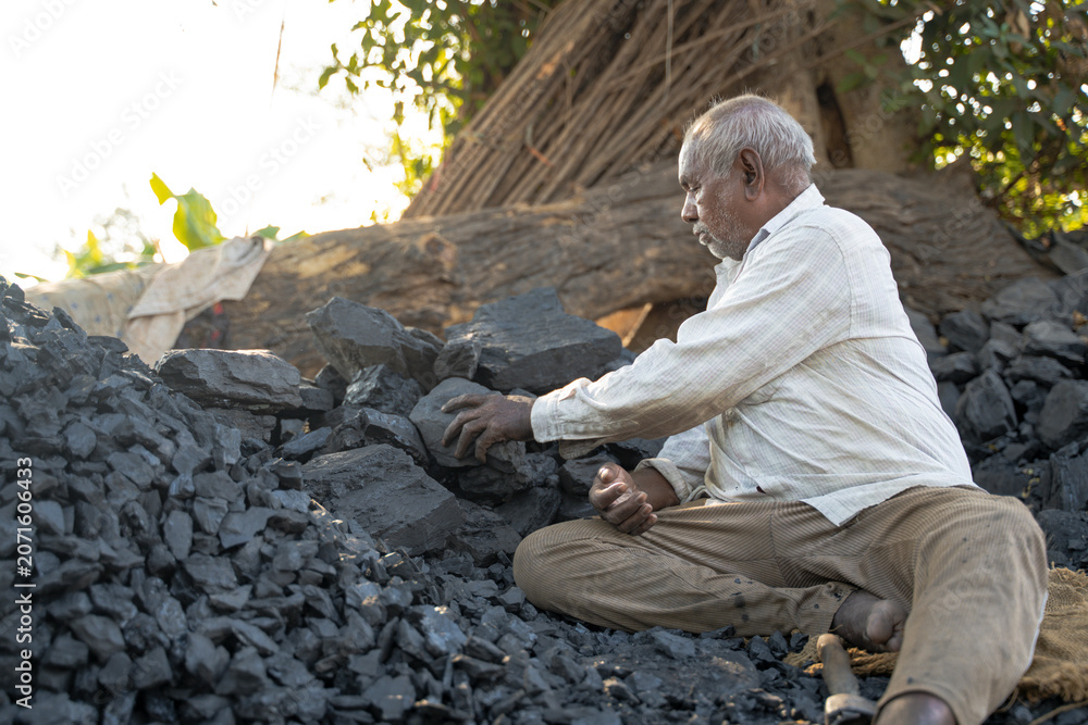 Fototapeta premium middle aged Indian villager man is working near black coal.