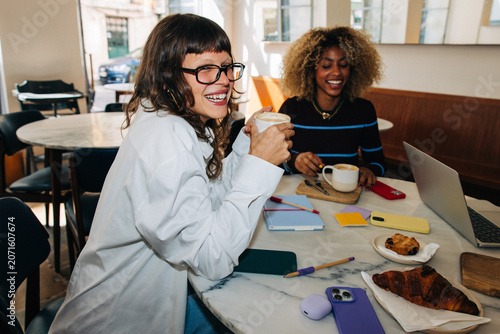 Two friends laughing over coffee and working in a café