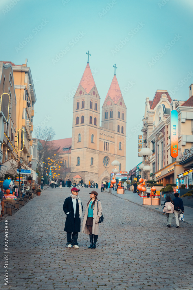 Naklejka premium Young couple standing on a historic European-style street with a church in Qingdao