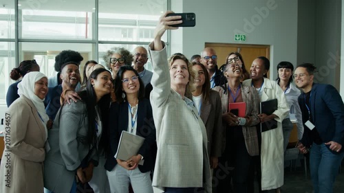 A cheerful group of colleagues and attendees happily pose for a group selfie at a conference or professional event. Their genuine smiles and laughter reflect a moment of positive connection.