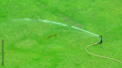 Canvastavla High-angle drone shot of a grassy field being irrigated by a rotating sprinkler, highlighting smart water distribution, sustainable landscaping, and consistent hydration for optimal lawn growth