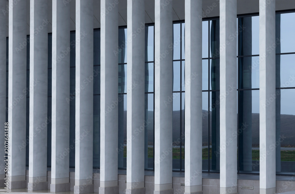 Naklejka premium Modern building facade with vertical white columns and dark glass windows. Repeating architectural lines create a clean contemporary exterior. Ideal