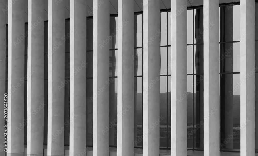 Obraz premium Modern building facade with vertical white columns and dark glass windows. Repeating architectural lines create a clean monochrome exterior. Ideal for
