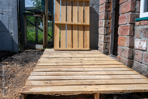 Valokuva a makeshift wooden pallet platform sitting on dirt near a brick building wall, w