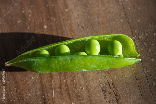 Canvas Print a single, freshly opened bright green pea pod revealing plump peas, resting on a textured wooden surface under dramatic natural sunlight