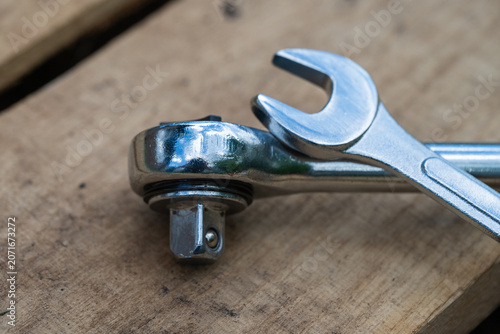 Fotografie a shiny chrome socket wrench and an open-ended spanner rest crosswise on a rustic, textured wooden surface