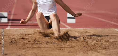 Female athlete long jump landing sand spray, landing in long jump in track and field