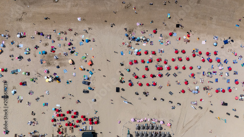 Top down aerial view of a busy sandy beach filled with colorful umbrellas, towels and sunbathers. Summer seaside scene showing people relaxing, beach tourism and vibrant vacation activity from above.