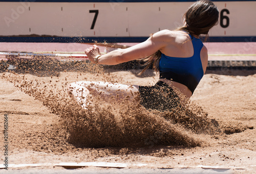 Female athlete long jump landing sand spray, landing in long jump in track and field