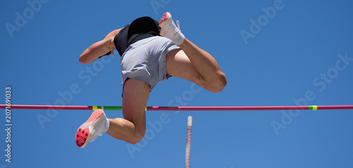 Athlete pole vault with a blue sky. Polevaulter pulling herself over the pole vault crossbar