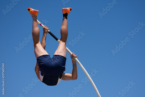 Athlete pole vault with a blue sky. Polevaulter pulling herself over the pole vault crossbar