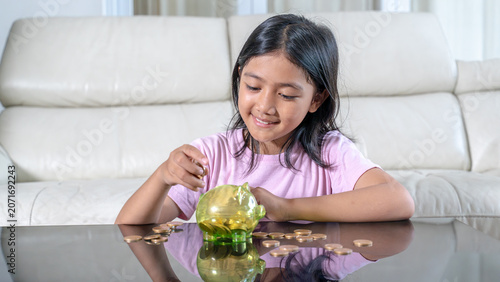 Smiling Young Asian Girl Putting Coins into a Piggy Bank to Save Money
