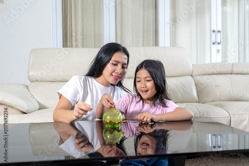 Asian Mother Teaching Her Young Daughter to Save Money with Piggy Bank