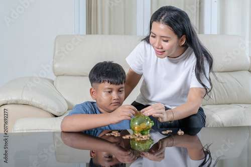 Asian Mother Helping Her Young Son Save Money with Piggy Bank at Home
