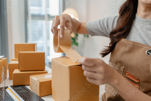 Small business owner packing customer orders, sealing shipping boxes, organizing parcels and managing ecommerce fulfillment in a home office while preparing products for fast and reliable delivery.