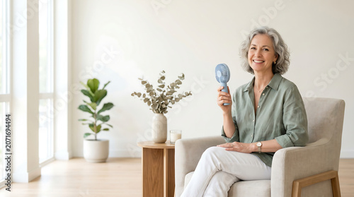 Smiling mature woman using portable misting fan for heat relief at home