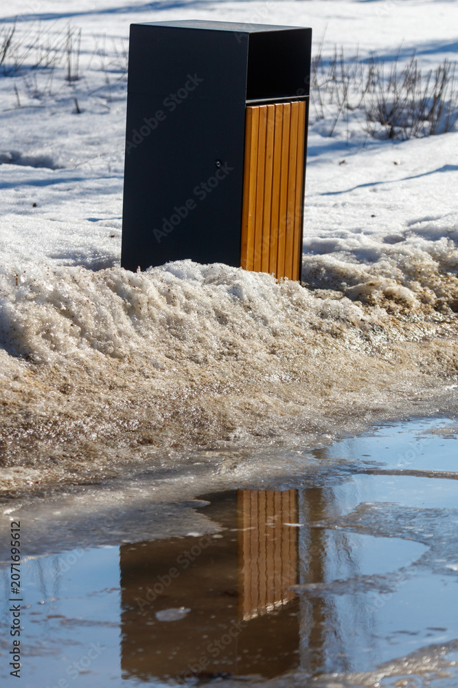 Fototapeta premium Black and wood trash bin stands in snowy field