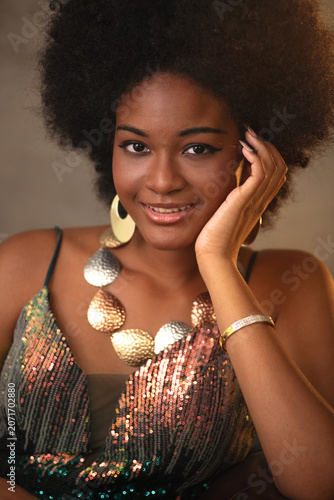 Close up image of an elegant African woman with an Afro hairstyle, wearing luxurious clothing and jewelry, smiling and looking at camera