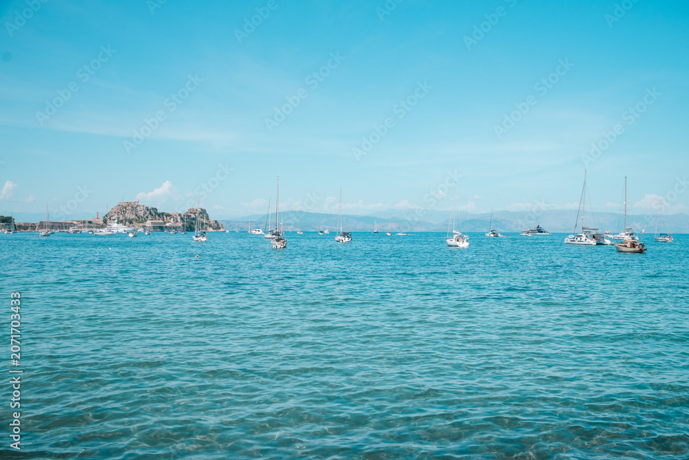 Obraz premium Sailboats Anchored in Turquoise Sea Near Corfu Old Fortress