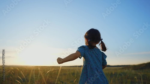 A girl is running through a field of grass during sunset. The girl appears joyful and carefree, moving towards the horizon under a clear sky.